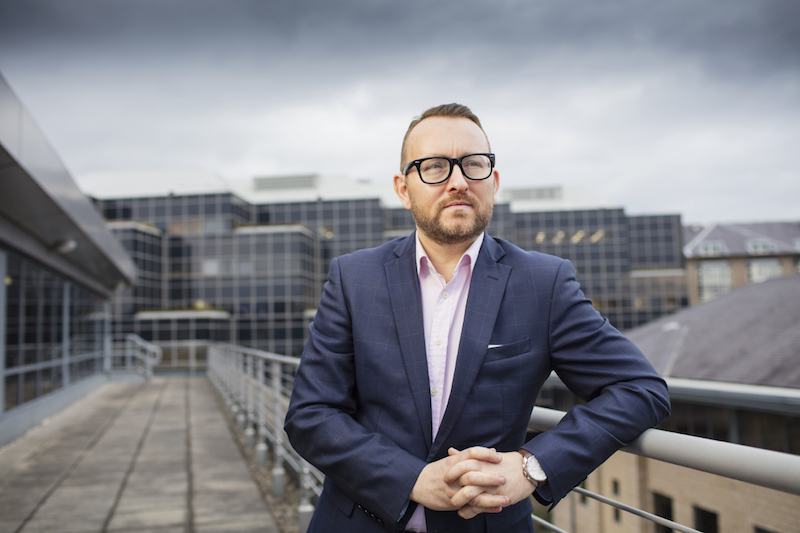 Corporate portrait of an executive standing on a rooftop terrace of an office building.