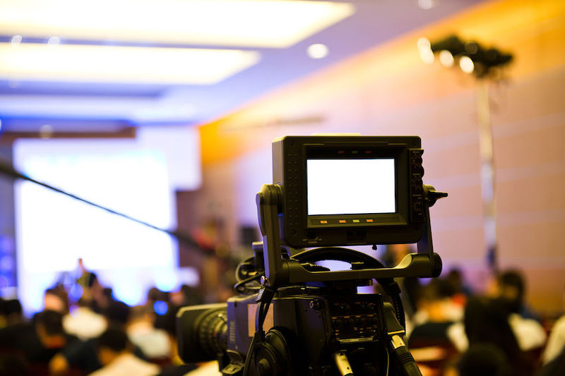 a video camera looking over the heads of an audience at a seminar